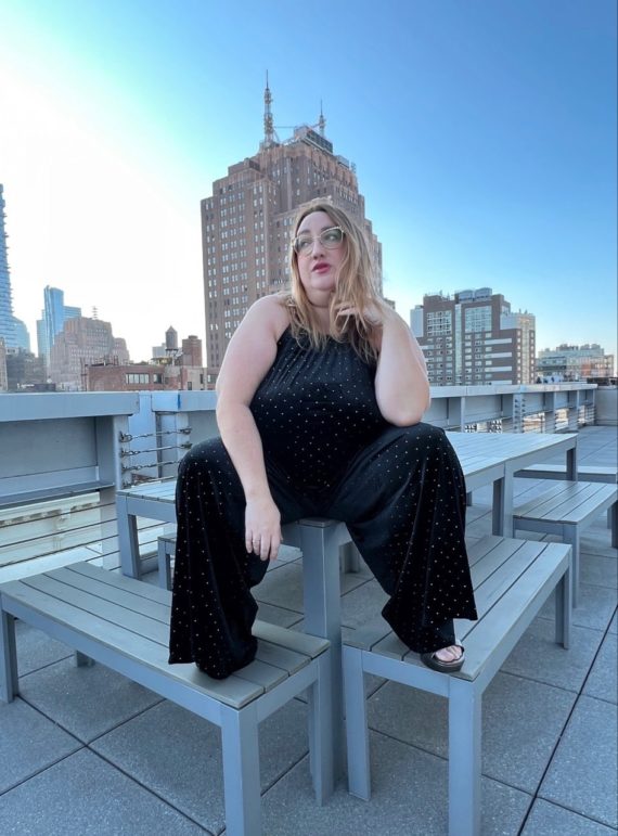 Photo of Sarah sitting on a table on a rooftop in a studded velvet jumpsuit