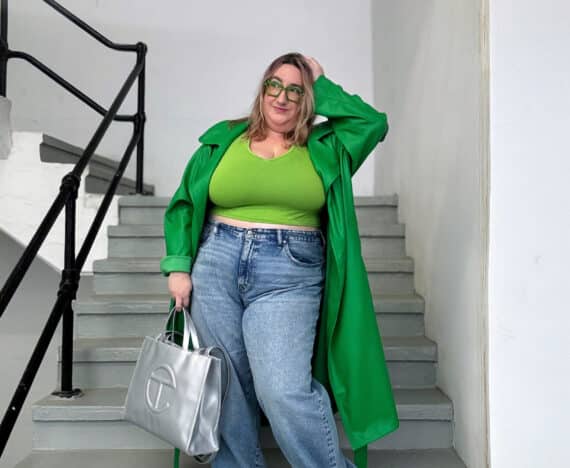 Sarah wearing a dark green faux leather trench coat, a light green crop top, plus size Madewell baggy jeans, a silver Telfar bag, and silver holographic chunky sneakers