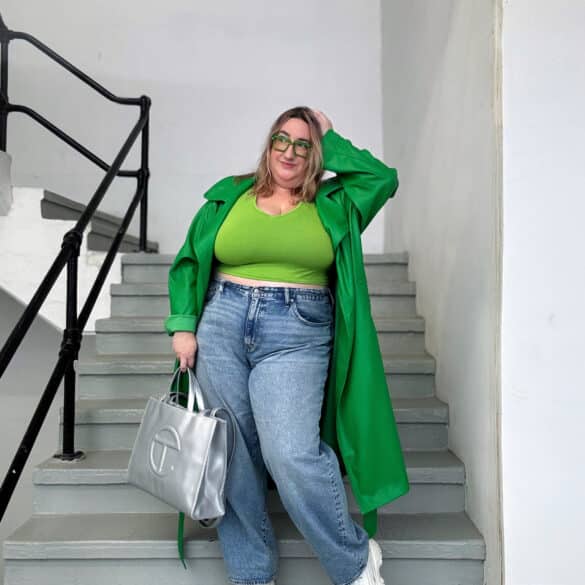 Sarah wearing a dark green faux leather trench coat, a light green crop top, plus size Madewell baggy jeans, a silver Telfar bag, and silver holographic chunky sneakers