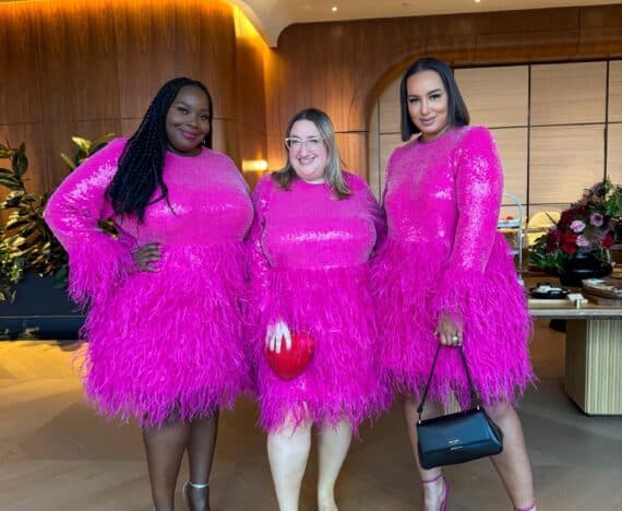 Sarah Chiwaya stands between fellow plus size style bloggers Alissa Wilson and Rochelle Johnson, all three wearing the pink sequined Kate Spade x Eloquii dress with feather trim